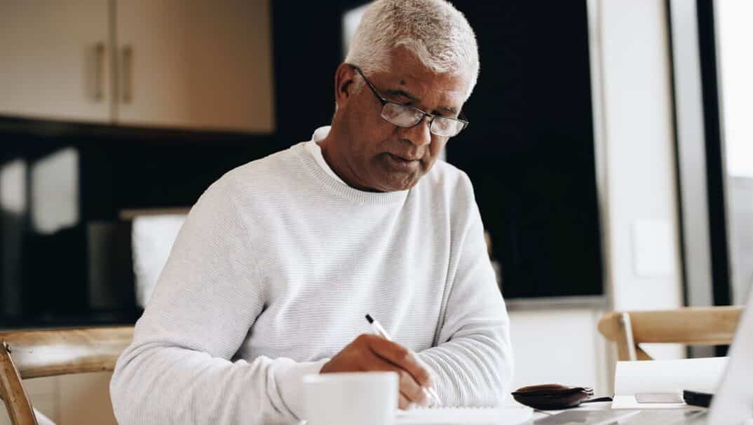 A middle-aged Black man sits at a table writing in a notebook.