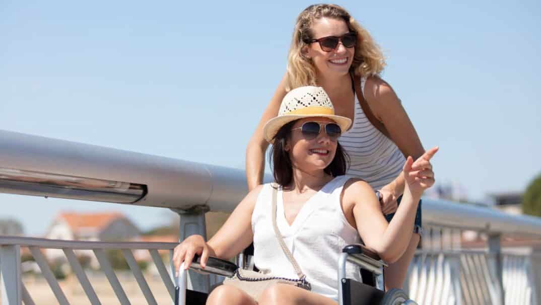 Two young women going up a boat dock. One woman is pushing the other in a wheelchair.