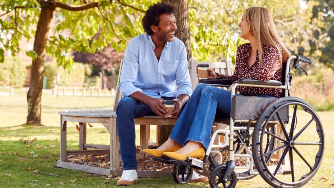 Woman in a wheelchair drinking coffee outside with her male friend