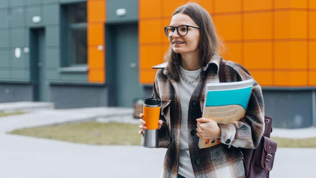 Young adult outside carrying coffee and school books