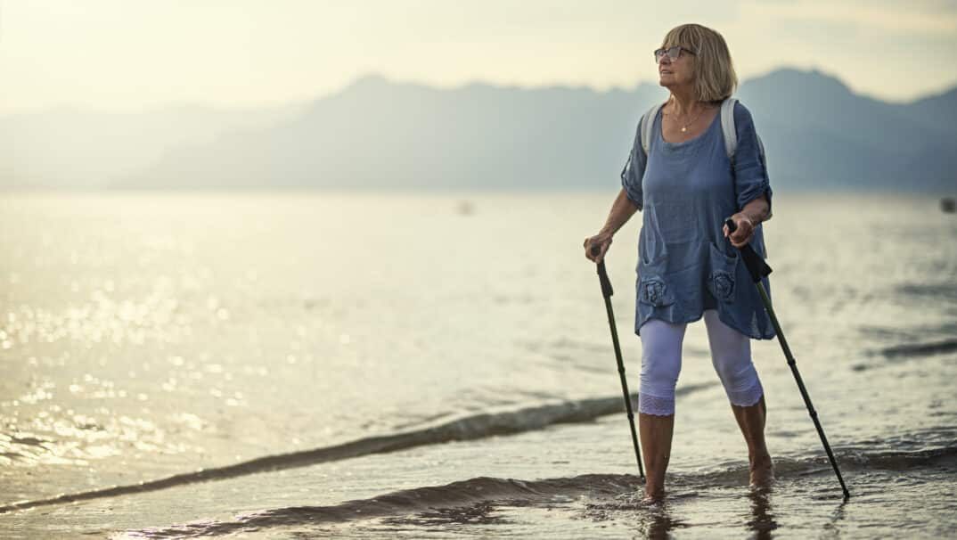 Woman walking on the beach with walking sticks