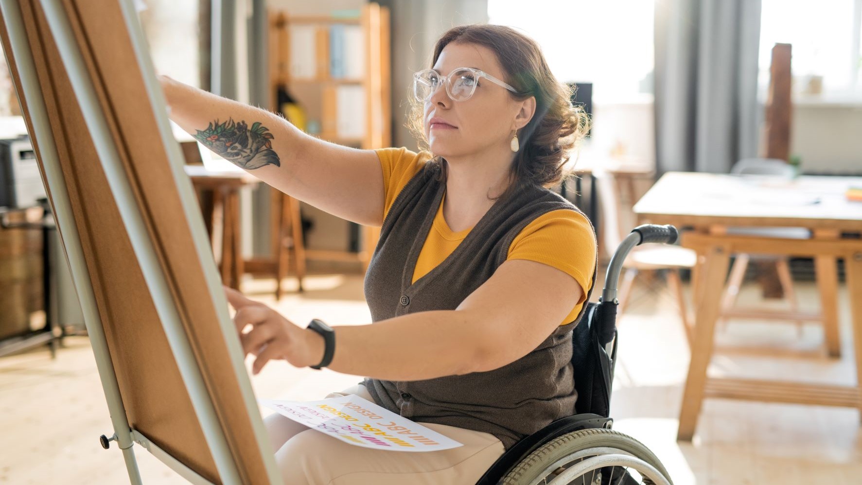 Woman in a wheelchair painting at an easle.