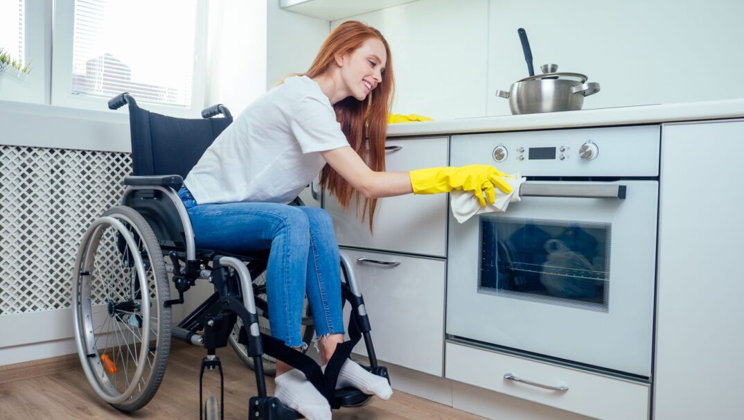 Young woman in wheelchair cleaning kitchen
