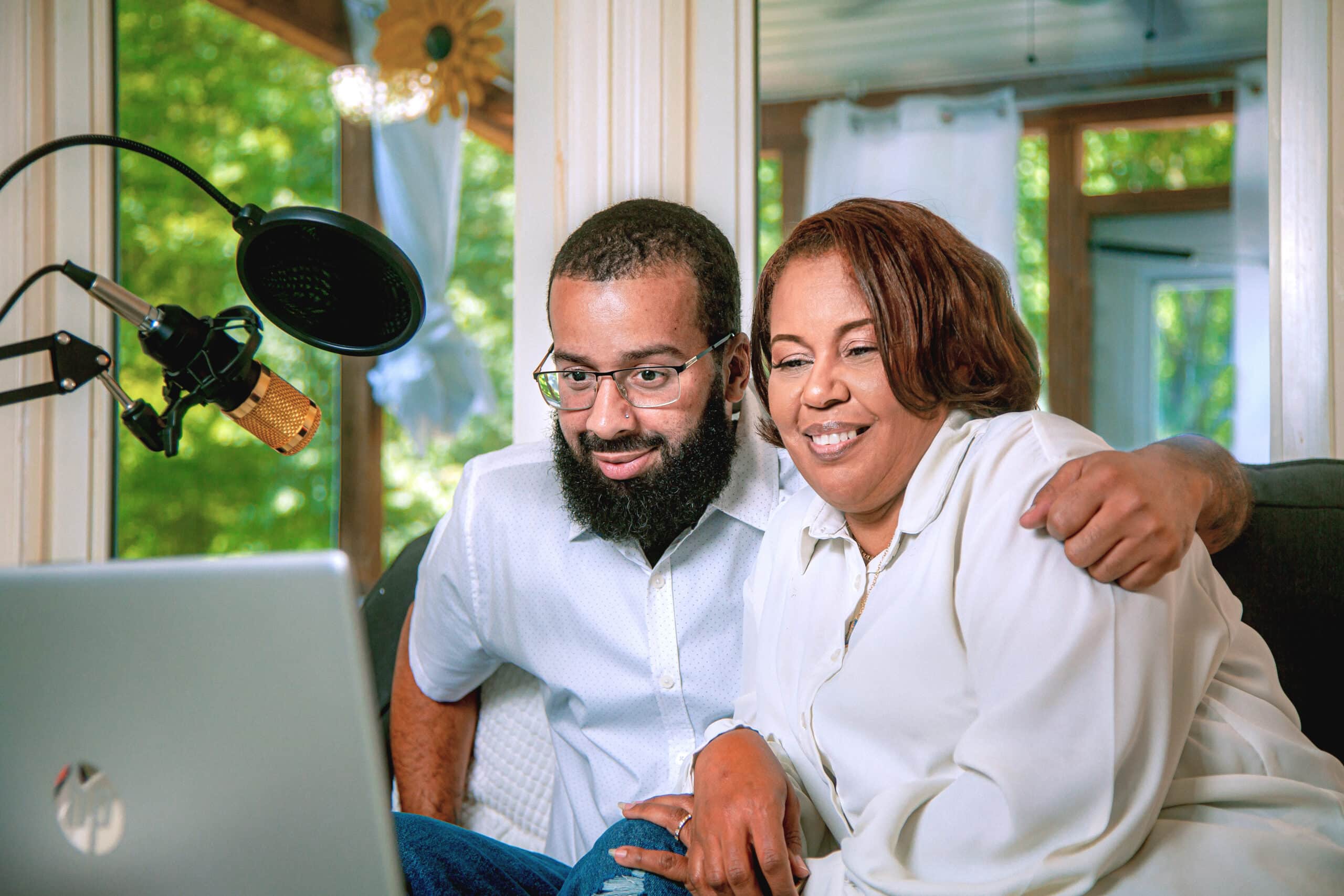 middle aged Black woman and her adult son smile together and look at laptop screen