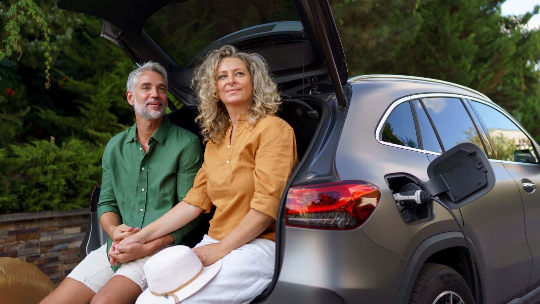 Couple sitting against trunk of car