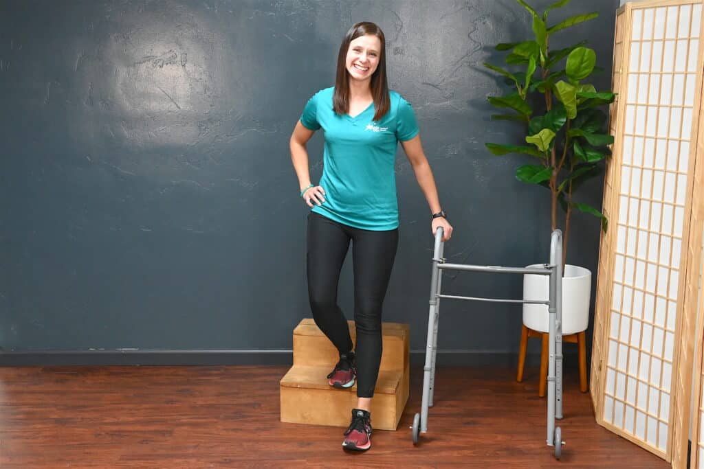 Physical therapist stands a step stool and a mobility aid while smiling