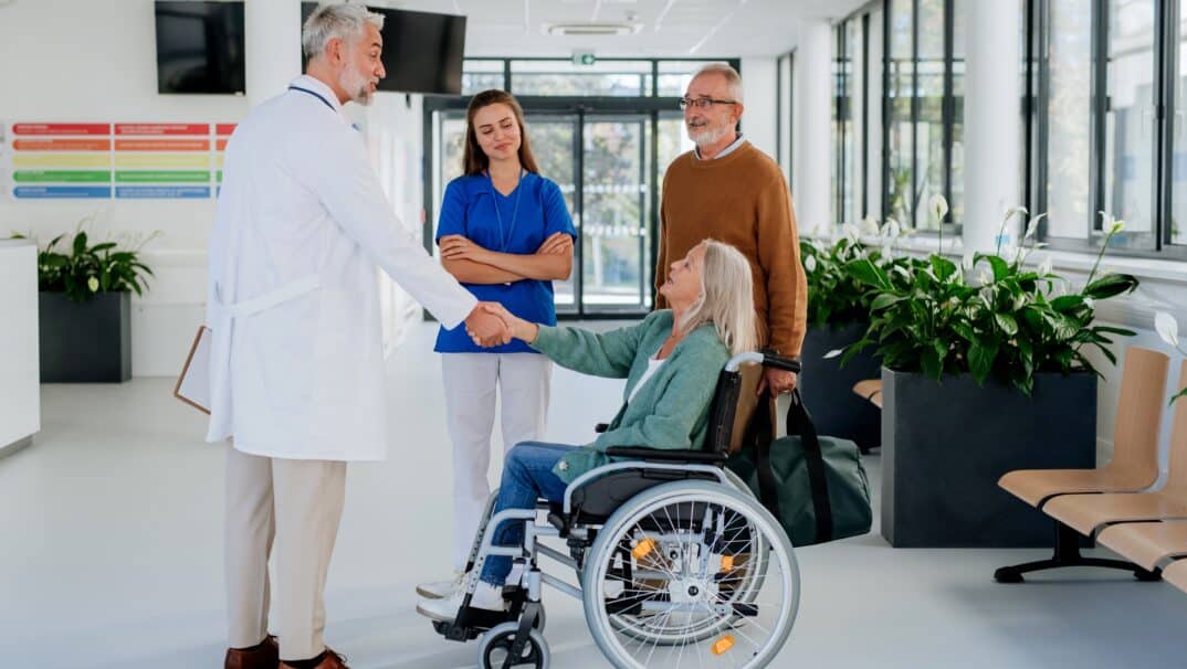 Two healthcare professionals with patient in a wheelchair and their support partner.