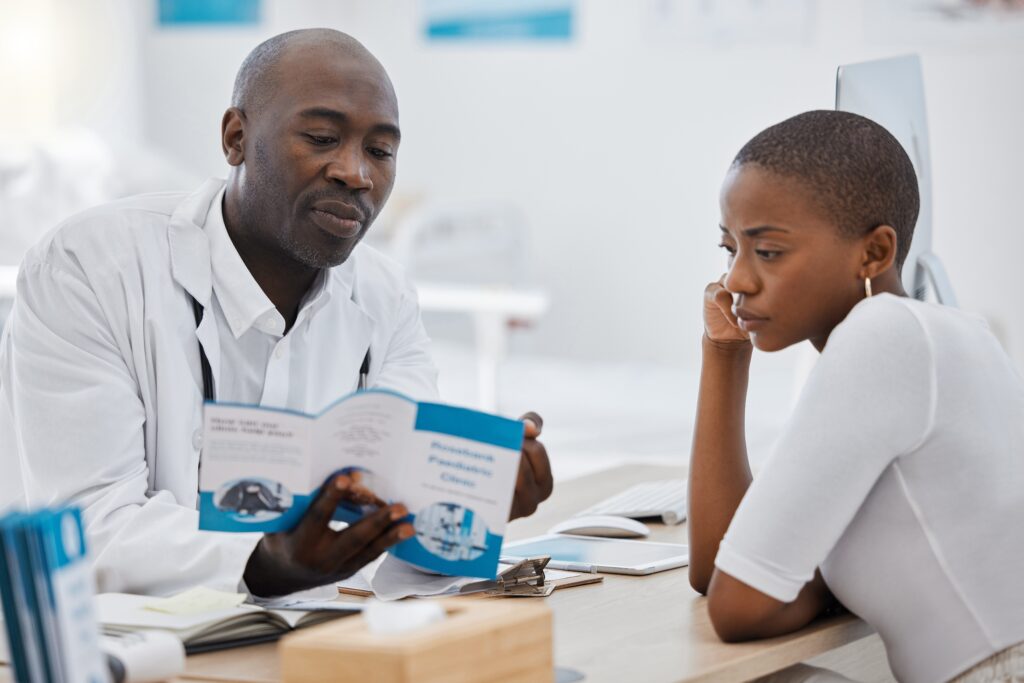 Doctor, brochure and medical patient consulting about health while learning about healthcare at office desk. Man, GP and support communication for woman on safety from virus, disease or sickness.