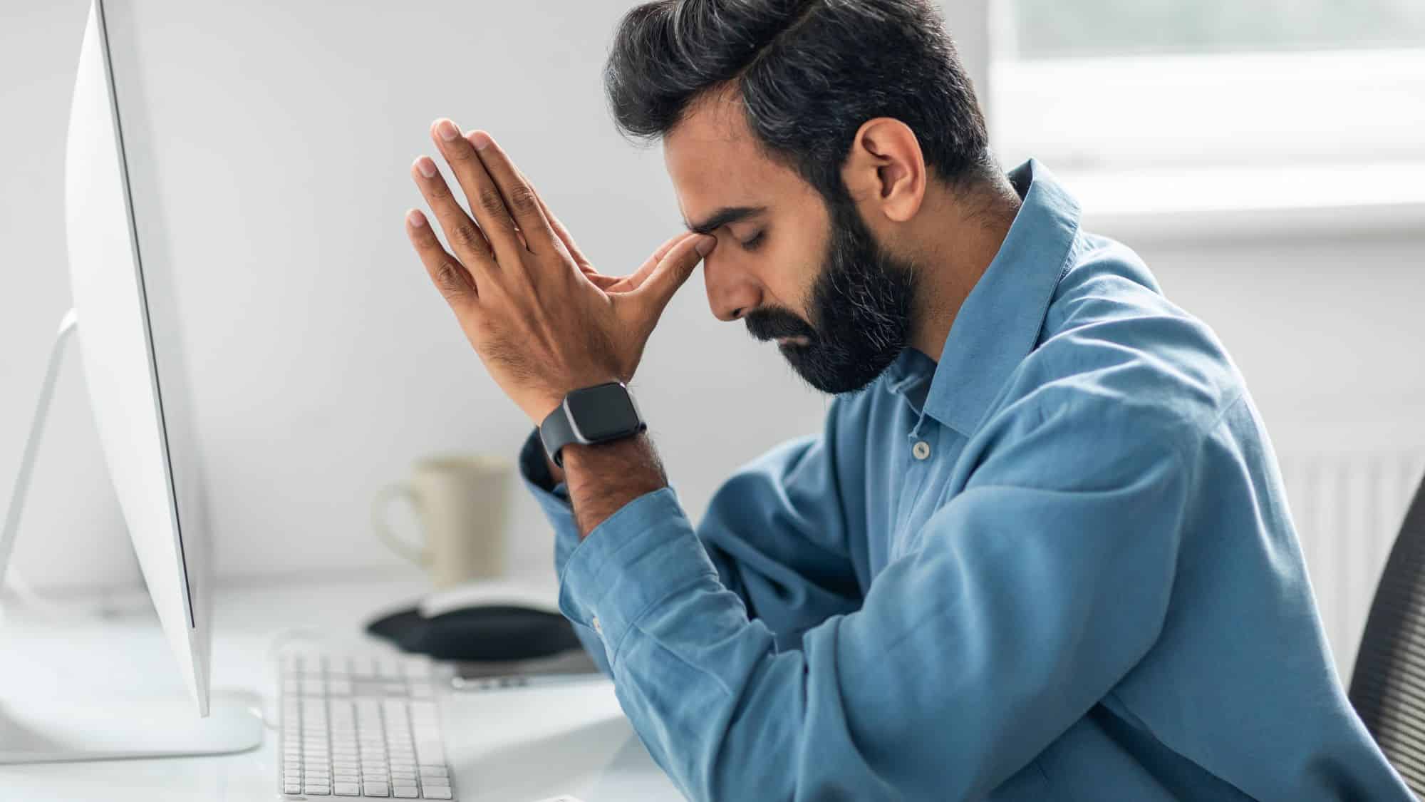 Man sitting at desk holding his head