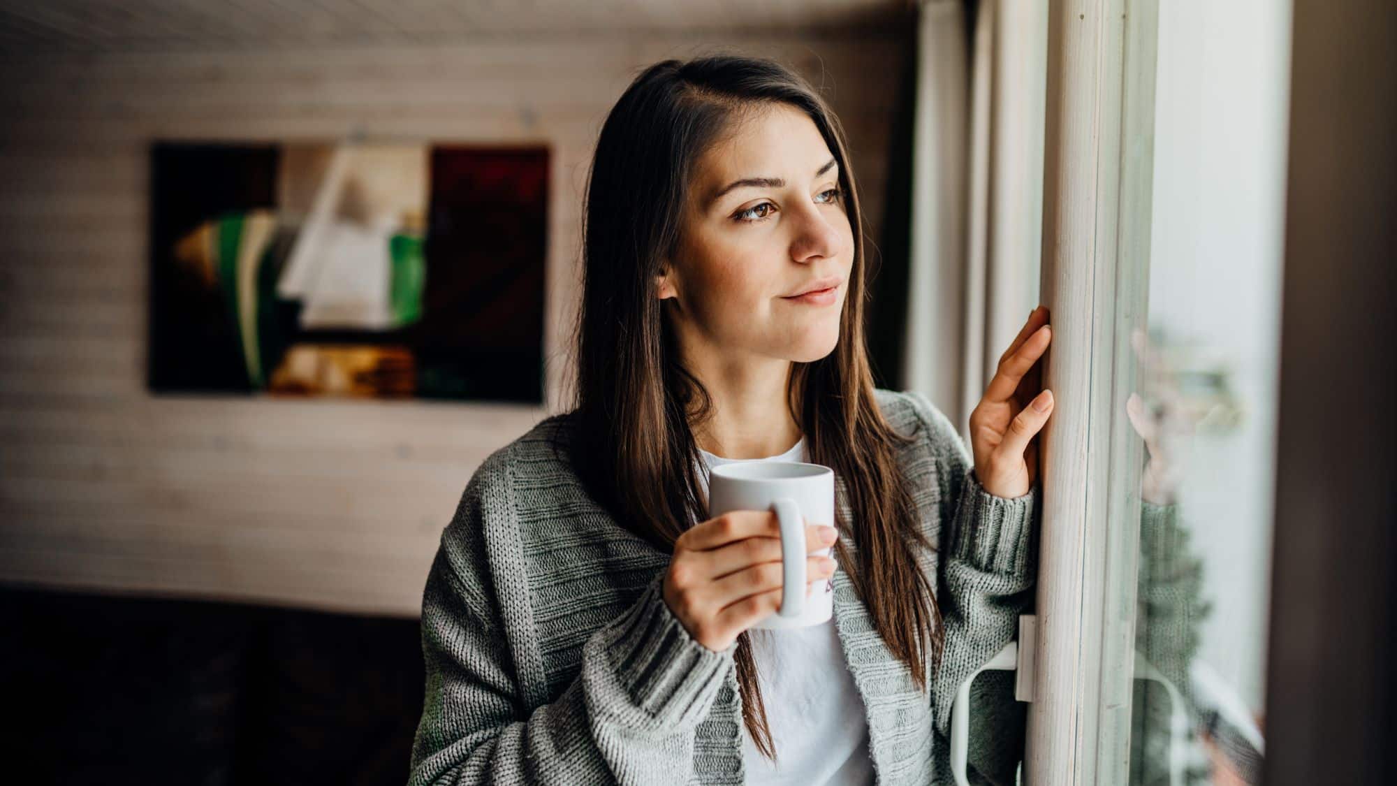 woman holding coffee mug staring out window