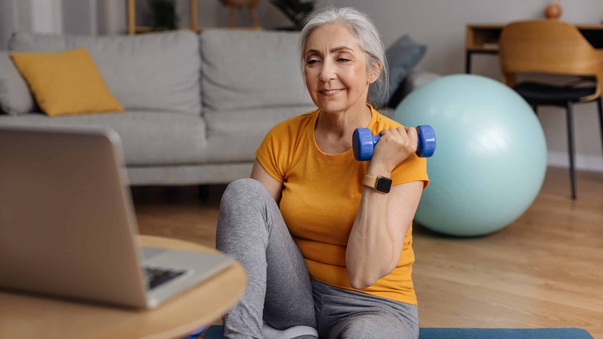 Older white woman doing a workout at her computer holding a weight