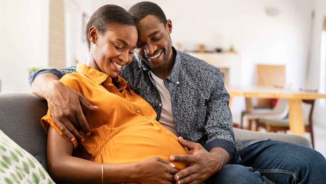 Black couple pregnant smiling at baby bump