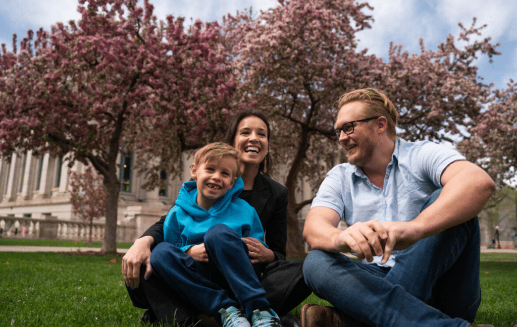 Julie, husband and son smiling while sitting on grass