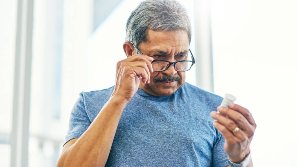 Elderly man with glasses looking at pill bottle