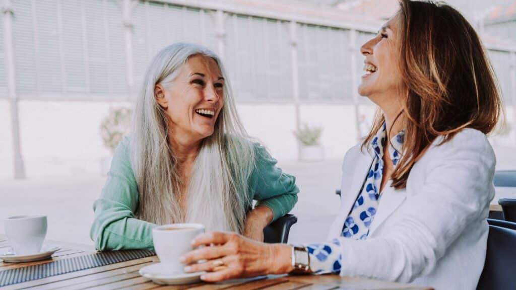 Two older women talking and laughing while drinking coffee