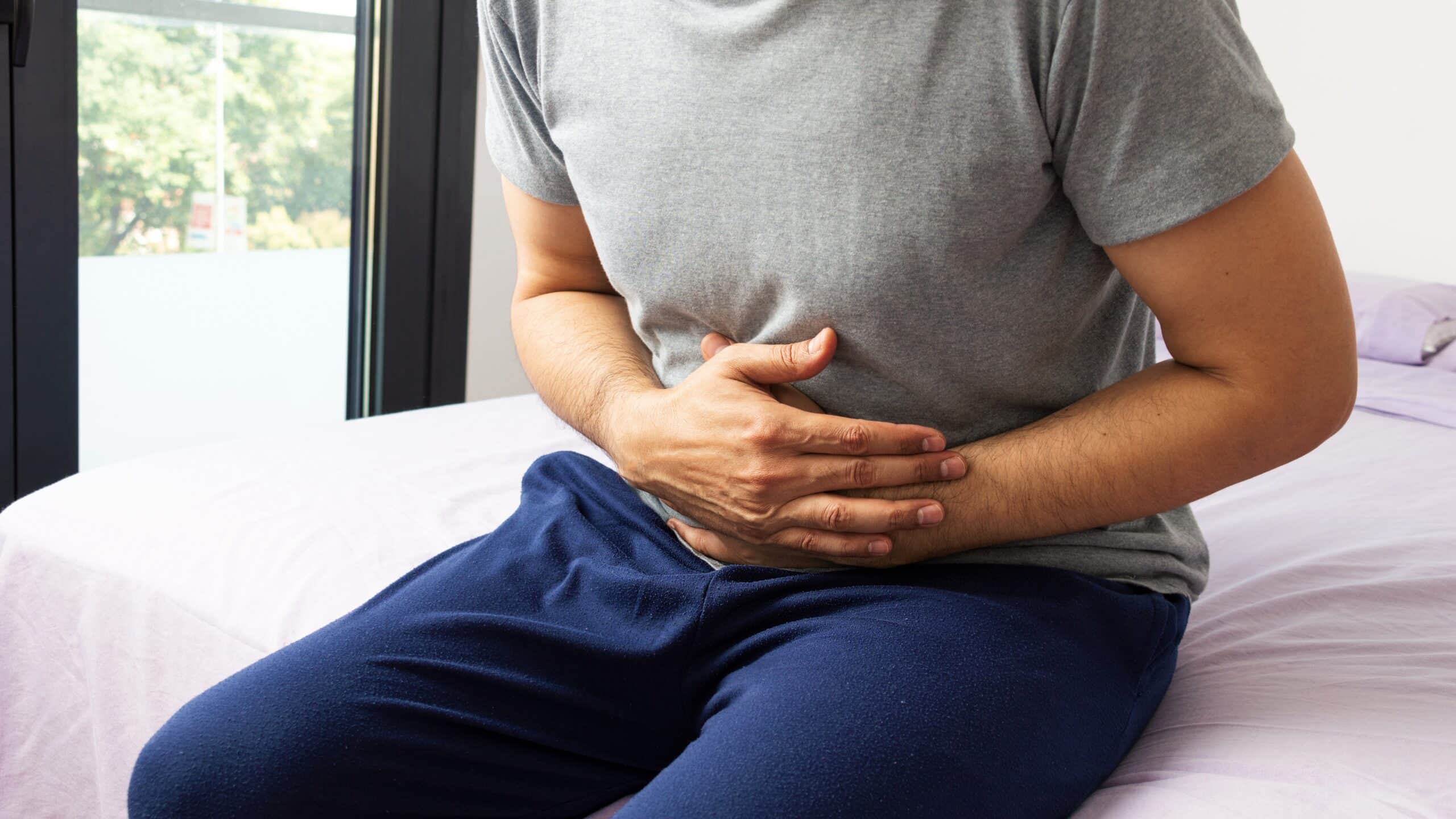 A man holding his mid section while sitting down on his bed.
