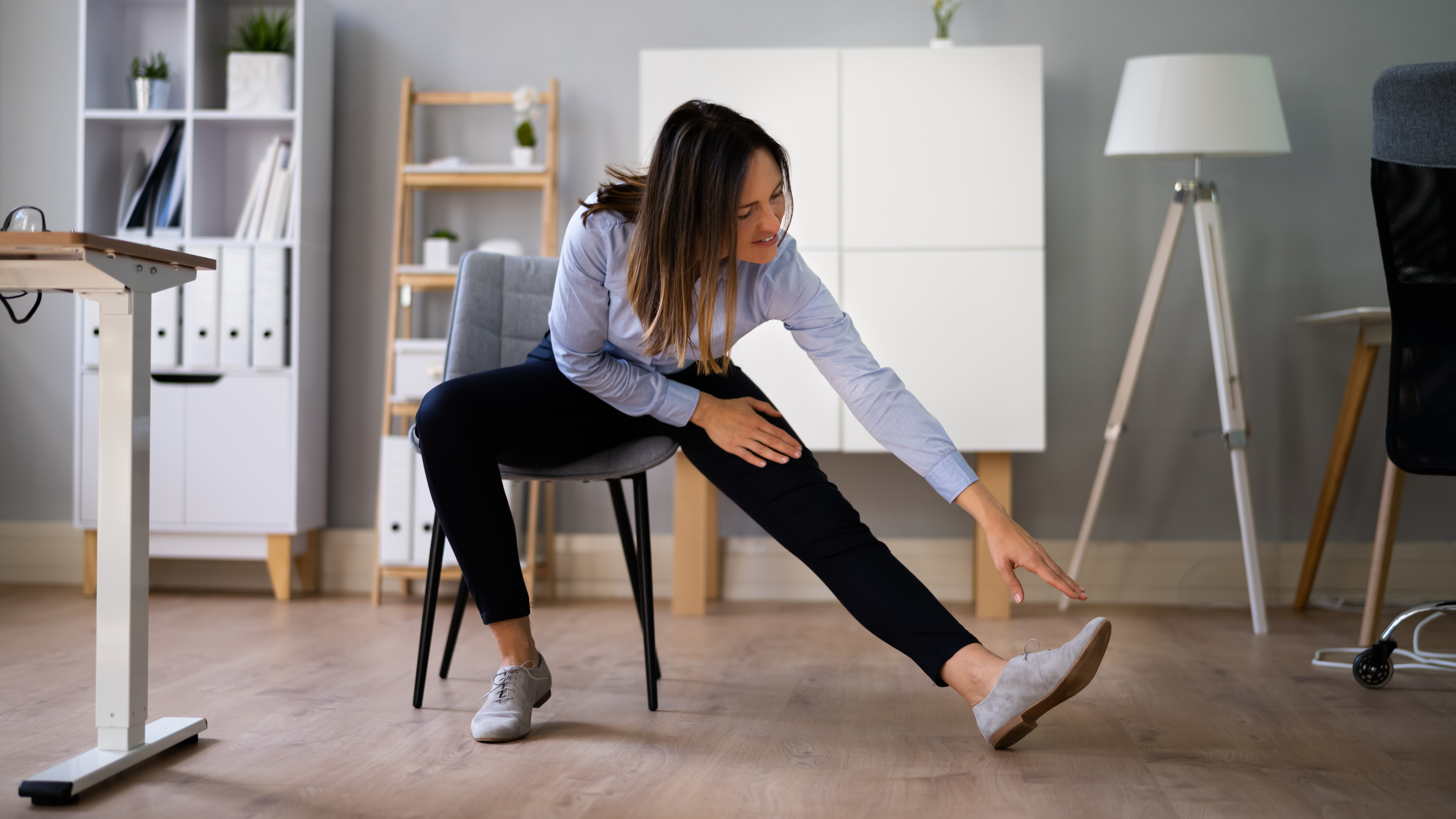 A young woman stretching her legs while sitting on her chair. She is in her office.