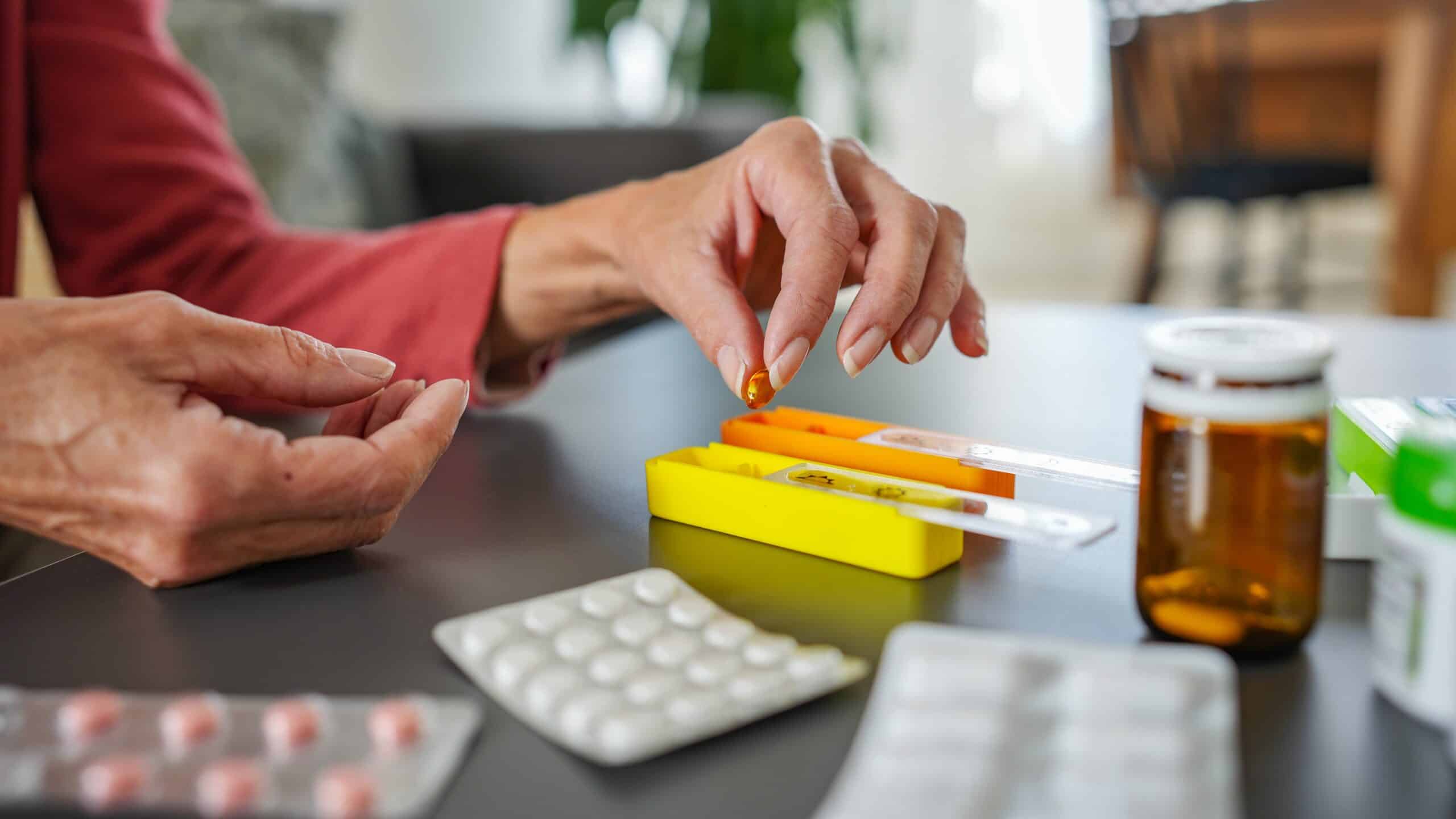 An elderly woman sorting various medications into her pill organizer. No face is shown.