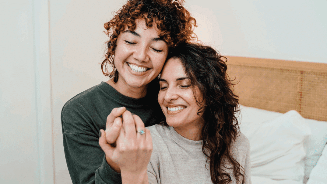 A lesbian couple smiles and holds hands