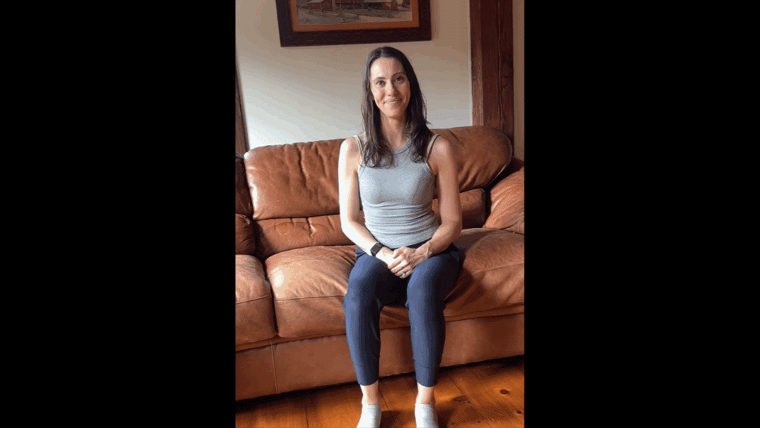 Courtney Capwell sitting on her couch demonstrating a stretch.