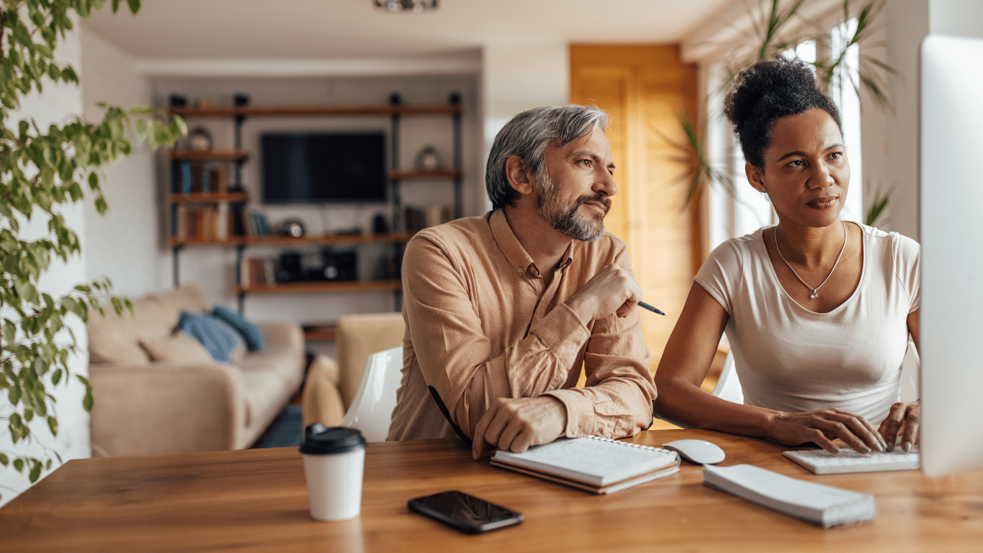 A couple looks together at a desktop computer screen. They are together at home.