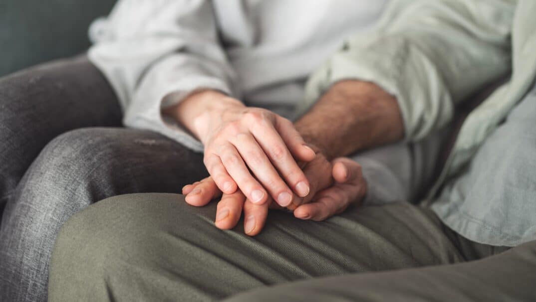 A couple holding hands sitting side by side. No faces are shown.