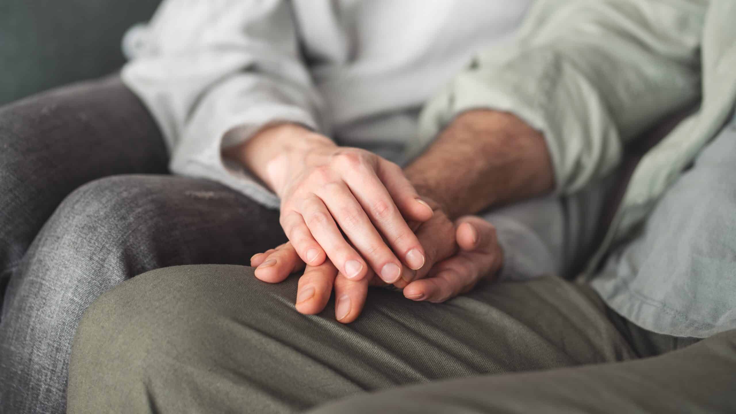 A couple holding hands sitting side by side. No faces are shown.