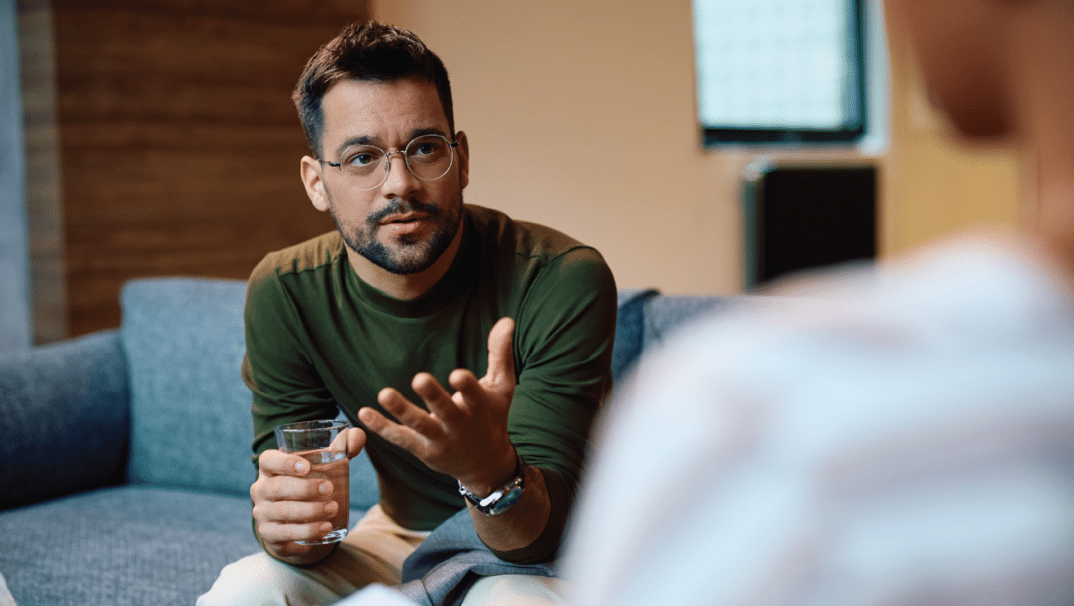 A man in glasses talks to his therapist, whose face is not showing.