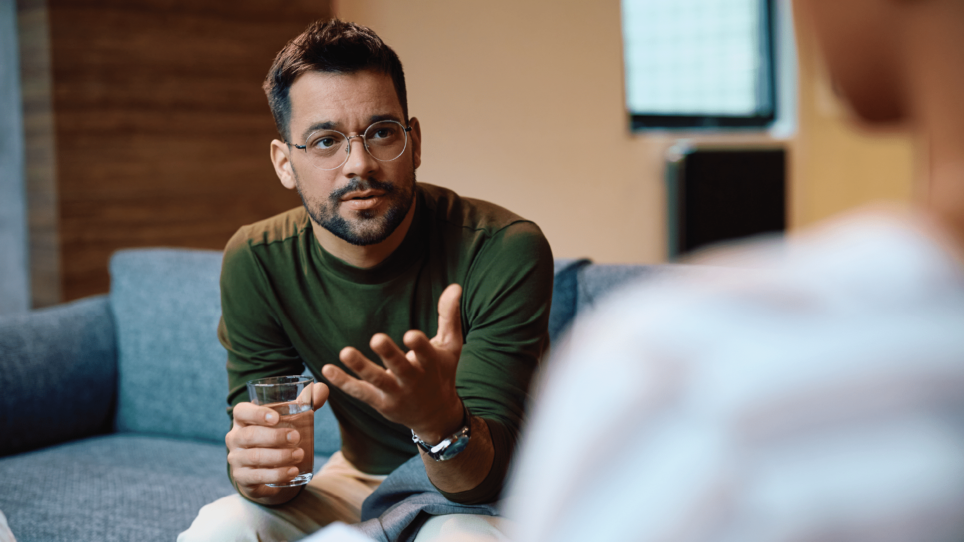 A man in glasses talks to his therapist, whose face is not showing.