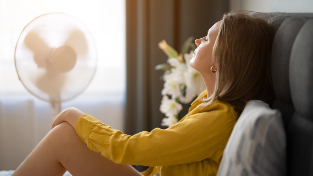 Woman in yellow sweater Sits In Front of Fan to stay cool.